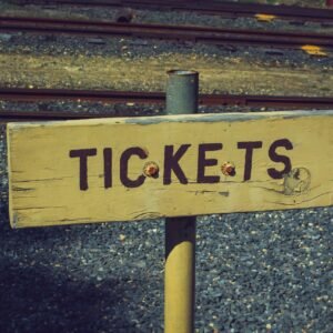 Weathered wooden ticket sign pointing towards railway tracks outdoors, vintage look.